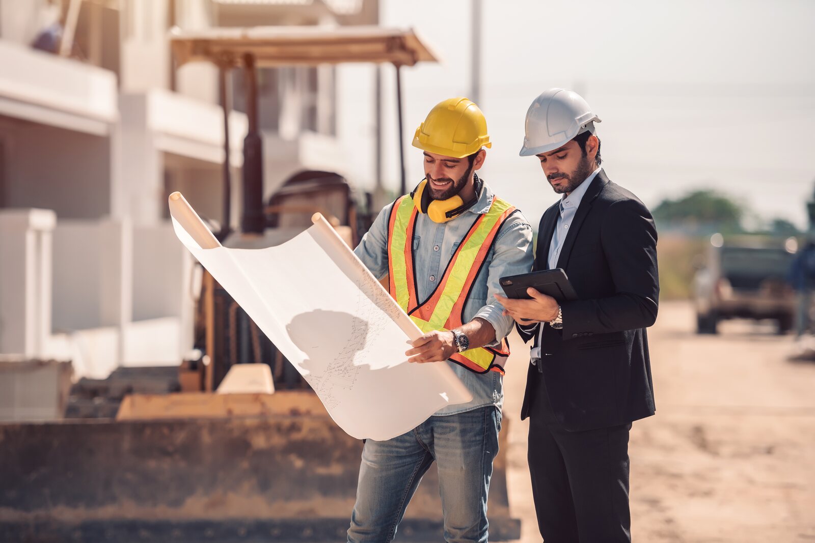 Operaio con elmetto e gilet ad alta visibilità e tecnico con tablet consultano una planimetria in cantiere